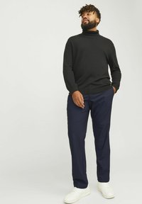 Schwarzer Rollkragenpullover mit langenÄrmeln, kombiniert mit marineblauen Hosen. Weiße Sneakers vervollständigen das Outfit, das einen lässigen Schnitt und eine glatte Textur aufweist.