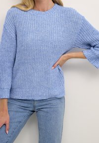 Light blue knitted sweater with a round neckline and ribbed cuffs. The fabric features a textured pattern and a relaxed fit design.
