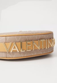 Brun läderväska med guld "VALENTINO"-logotyp. Har en slät yta och en strukturerad form, kompletterad med ett kontrasterande gult rand.