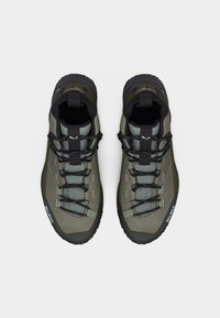 Ζευγάρι πεζοπορικών παπουτσιών ελιάς με μαύρα κορδόνια και μαύρες σόλες, απεικονισμένα από ψηλά σε λευκό φόντο.