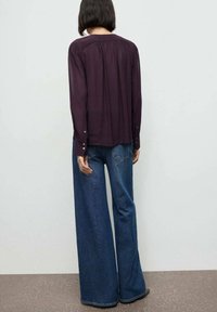 Langærmet, mørk lilla bluse med plisseret rygdesign, parret med bredbenede, falmede blå denimjeans i klassisk femlommesstil.
