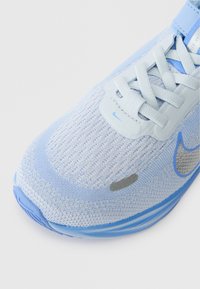 Jasnoniebieski sportowy but z teksturowanej siateczki, syntetycznymi akcentami i okrągłym noskiem. Zawiera szczegóły logo w kolorze szarym oraz sznurowaną zapięcie.