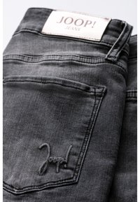 Tmavě šedé džíny z denimu s viditelným zadním kapesem, na kterém je vyšitá značka „Joop!“. Na pase je umístěna štítek s logem značky.