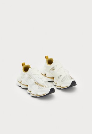 Witte sport schoenen met een textuur mesh bovenwerk, benadrukt door gouden accenten, een verstelbare band en een dikke gevoerde zool.