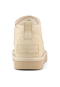 Botines de ante beige con un acabado texturizado, forro textil, tacón corto y una tira en la parte trasera. Presenta un grabado de la marca en el tacón.