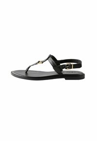 Sandalia de cuero negro con suela plana, diseño de tira en forma de T, acento de hardware en tono dorado y correa ajustable en el tobillo. Textura suave.