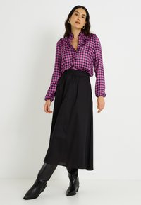 Blusa a cuadros en tonos rosa y negro con cuello rizado, combinada con una falda maxi negra y fluida y botas de tobillo negras. Textura de tejido suave.