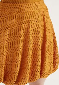 Gonna arancione con motivo a zig zag testurizzato, caratterizzata da una vita elastica ampia e una silhouette svasata. Realizzata in un tessuto intrecciato.