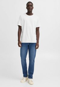 Camiseta de algodón blanca con cuello redondo, combinada con jeans de denim azul. El conjunto se complementa con zapatillas de color claro.