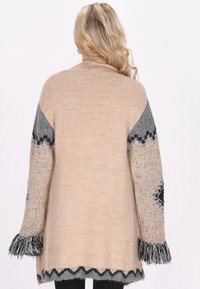 Stickad cardigan i beige och grått, med långa ärmar, strukturerade mönster, fransade manschetter och en zigzag-nederkant.