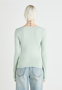Langermet topp i myk, lys grønn stoff med en tettsittende design. Glatt tekstur og rund halslinning. Synlige sømdetaljer på baksiden.
