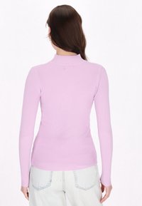 Maglietta a maniche lunghe in maglia a coste di color lavanda con collo alto; presenta una silhouette aderente e una texture liscia, abbinata a pantaloni in denim chiaro.