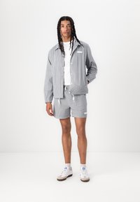 Stripet jakke og shorts i grå og hvid, lavet af letvægtigt stof. Har snoretræk i taljen, frontknapper og kontrasterende detaljer.