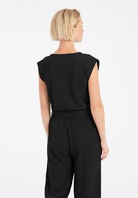 Zwart overall met korte mouwen, textuurstof, bijpassende riem in de taille, losse broekspijpen en een wijde halslijn.