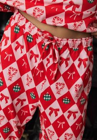 Pantalon de pyjama rouge avec un motif en diamant, ornés de décorations vertes, de cannes en sucre et de nœuds. Tissu doux avec une taille élastique et un cordon de serrage.