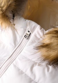 Chaqueta puffer blanca con capucha forrada de piel, que presenta un cierre visible y una etiqueta de marca. El tejido parece suave y tiene costuras acolchadas.
