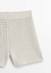 Light gray knit shorts with a textured, open weave pattern and a soft, elastic waistband. Hem is rounded at the leg openings.