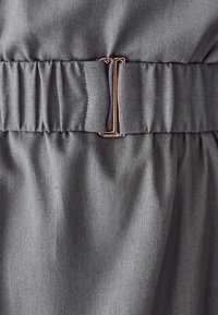 Detalle de tela gris con textura arrugada y una hebilla de metal dorado, que presenta un acabado suave y un sutil brillo.