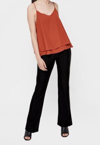 Rdzawoczerwony, bezrękawnik o warstwowej konstrukcji. W połączeniu z czarnymi, dopasowanymi, lekko rozszerzanymi spodniami i czarnymi szpilkami z odkrytymi palcami.