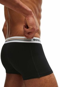 Svarta boxershorts med vit midja som har svarta och bruna ränder samt "BOSS"-logotypen. Slät väv och figurnära design.
