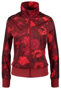 Czerwona kurtka na zamek z kwiatowym wzorem, wysokim kołnierzem i czarnymi paskami po bokach. Materiał wydaje się lekki z prążkowanymi mankietami i dołem.