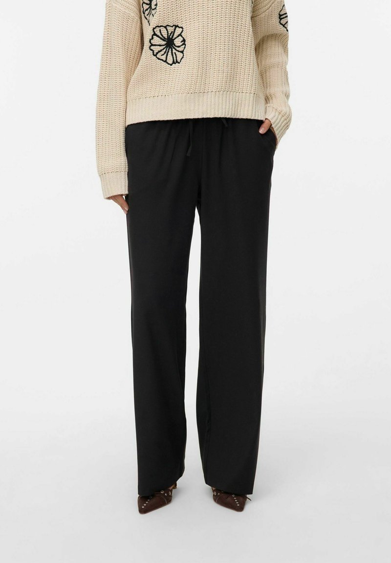 Pantalon noir à jambes larges avec une taille élastique. Texture lisse, coupe ajustée. Associe à un pull en tricot beige avec des broderies florales.