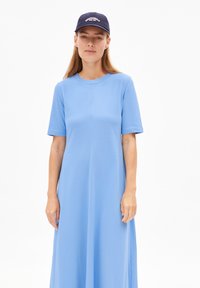 Robe courte bleu clair à manches courtes en tissu doux, avec un col rond et une coupe droite et ample. Portée avec une casquette navy.