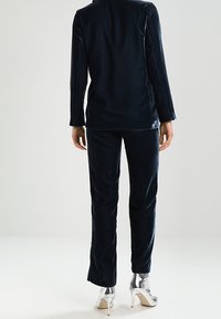 Námořnicky modrý sametový dvoudílný outfit s dlouhým rukávem a rovnými kalhotami, doplněný lesklými stříbrnými lodičkami.