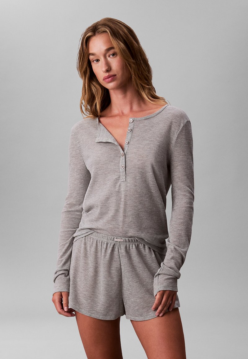 Grijs top met lange mouwen en knoopsluiting, met een ontspannen pasvorm, gecombineerd met bijpassende grijze korte broek met elastische tailleband voor comfort.