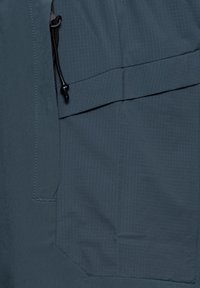 Nærbillede af mørkegråt stof med gittermønster og sort justeringssnor på en lommeflap.