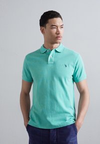 Turkos polo-shirt i mjuk bomull, med klassisk krage, tre-knappsknäppning och en liten broderad logotyp på bröstet.