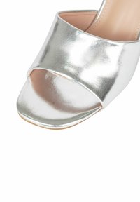 Sandalo aperto in toe di metallo argentato con una fascia larga, texture liscia e suola piatta. Nessun abbellimento o motivo visibile.