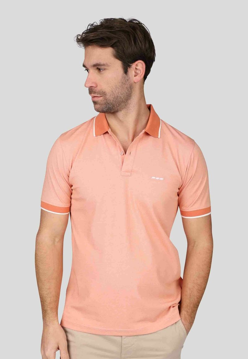 Polo rose clair avec un col orange et des accents blancs. Manches courtes avec un bandeau assorti aux poignets. Le tissu semble lisse.