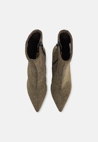 Spisse tøfler med ankelhøyde i metallisk gullstoff, med en glatt tekstur og glidelåser på siden for lukking, med en tettsittende design.