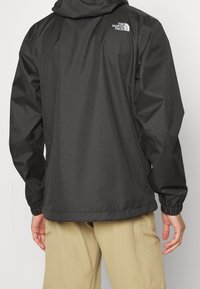 Water-resistant black jacket with a hood, elastic cuffs, and The North Face logo on the upper back. Smooth texture and lightweight design.