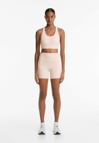 Ljusbeige sportbehå och shorts set i stretchigt tyg, med en sömlös design och en mjuk textur utan synliga mönster.