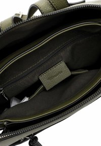 Interno di una borsa in pelle verde oliva con una tasca con zip e due scomparti. Cerniera e cuciture nere, texture liscia e etichetta del marchio visibile.