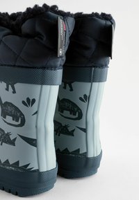 Granatowe buty z teksturowanymi, ciemnoszarymi gumowymi podeszwami mają wełnianą mankiet oraz zabawne wzory dinozaurów na jasnoszarej powierzchni.