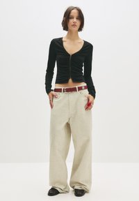 Top nero a maniche lunghe con design aderente e arricciato, chiusura con bottoni, abbinato a pantaloni larghi, chiari e testurizzati e una cintura rossa.