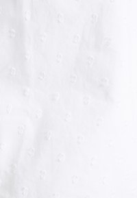 Tissu blanc avec un motif texturé de petits points en relief uniformément espacés, en coton doux. Finition lisse avec un éclat minimal.