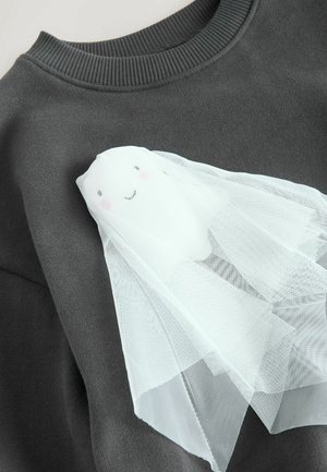 Sweatshirt gris avec un design de fantôme blanc ayant un visage souriant, agrémenté d'un tissu en tulle pâle tombant comme un voile, texture douce.