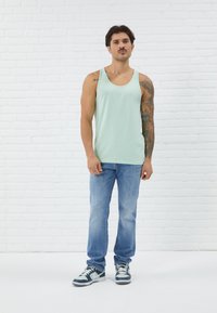 Světle mátově zelený tílko, džíny a šedé tenisky. Tílko má kulatý výstřih a outfit má pohodlný střih.