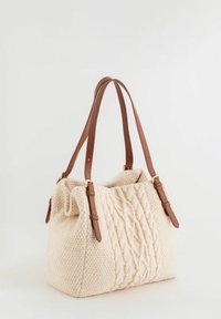 Bolso de mano de punto crema con textura trenzada, con correas de hombro de cuero marrón y detalles en metal dorado. Diseño suave y funcional.