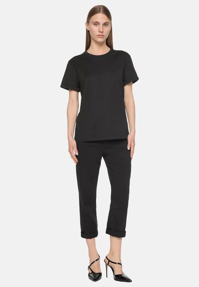 Camiseta de algodón negra de manga corta, combinada con pantalones negros enrollados y tacones altos negros brillantes, creando un look monocromático.