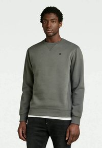 Sweatshirt cinza de gola redonda em material suave, com bainha e punhos canelados, apresentando um pequeno logo no lado esquerdo do peito.