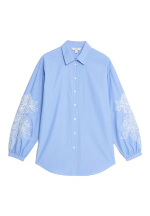 Camicia a righe blu chiaro con colletto a punte, chiusura con bottoni e maniche lunghe a sbuffo, con ricami floreali bianchi ai polsini.