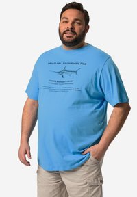 Camiseta de algodón azul claro con un estampado gráfico negro que incluye texto e ilustración de un pez en el frente. Manga corta y escote redondo.