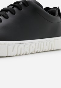 Baskets en cuir noir avec lacets noirs et semelle blanche embossée du texte "MOSCHINO" sur le côté.