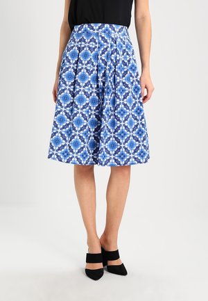 Woman wearing a knee-length blue and white geometric patterned skirt, black sleeveless top, and black pointed-toe block heels.