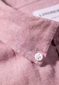 Zalmkleurig linnen shirt met kraag met subtiele textuur, voorzien van een witte knoop en nette stiksels langs de rand. Etiket gedeeltelijk zichtbaar.